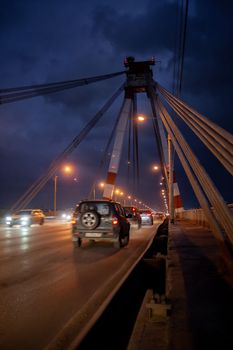 29.11.2022, Cherepovets, Russia. A large automobile bridge on which cars drive at night. A bridge with large columns and lighting. Cars are driving over the bridge