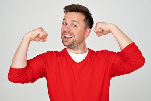 Young handsome man showing arm muscle, confident and proud of power. Studio shot