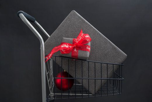 Christmas gift boxes in black paper in a shopping basket with red balls on a black background. High quality photo