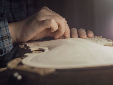 artisan working on raw wood violin plate with finger plane on the bench