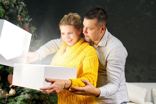 Man giving a Christmas present to his girlfriend. Great xmas surprise Beautiful young woman opening a gift box and smiling while her boyfriend hug her. Christmas wonder concept