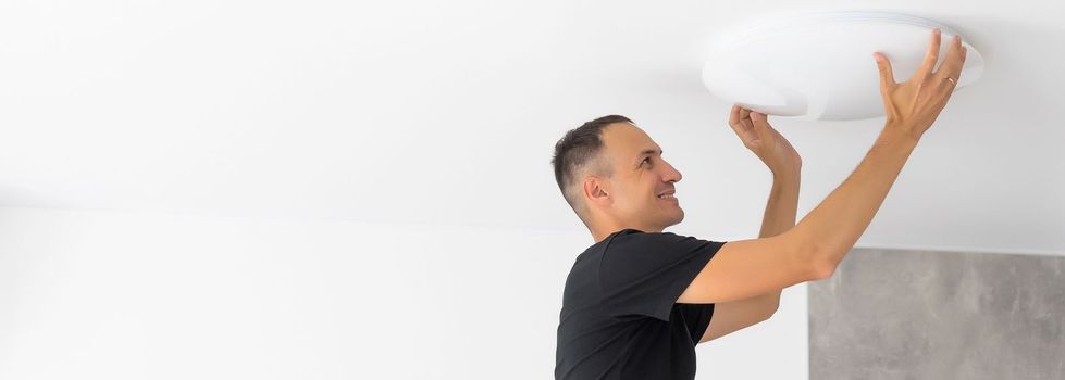 Worker repairing lamp on stretch ceiling indoors.