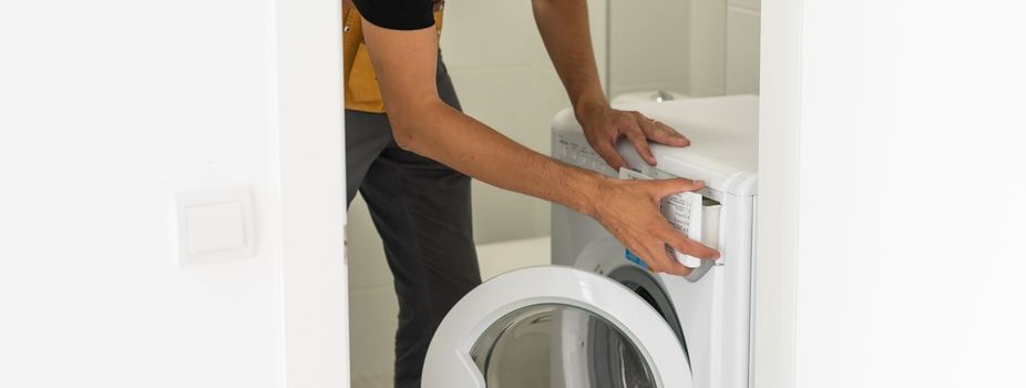 Young attractive smiling worker in uniform fixing washing machine