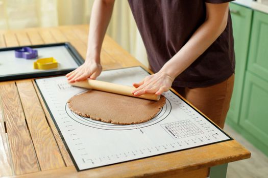 Woman's hands roll out gingerbread cookie dough on silicone baking mat.