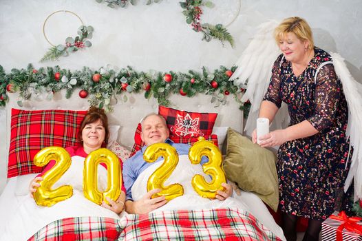 beautiful couple laying in bed, planning to have a baby. Christmas and happy New Year wishes with numbers 2023. Woman with angel wings, Christmas wonder.