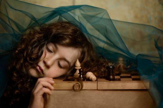 a girl with dark curly hair in a dark dress fell asleep while playing chess right on the chessboard and in her dream she thinks about the next move, picking up a chess piece. High quality photo