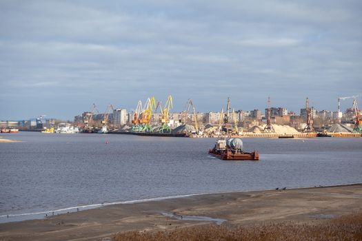 River port. Port cranes on the bank of the river. Embankment of the river port, a barge at the quay wall. Large port cranes on the river. Extraction and transportation of sand other cargo