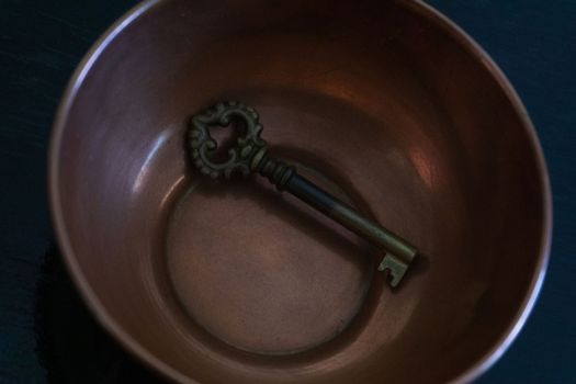 Antique metal key in antique copper bowl close up