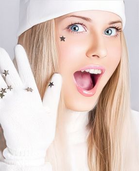 Greetings from a woman in a white hat and gloves and a merry holiday season. Beautiful female model against studio background at festive event. Laughing and loving the lifestyle of the holidays, surprised blonde girl smiles.