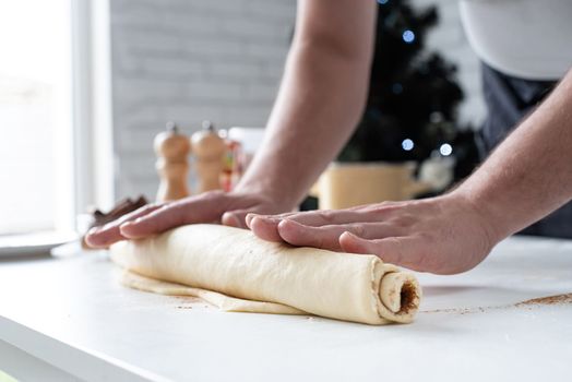freshly made cinnamon rolls on the baking tray, christmas tree with lights on the background, festive cooking