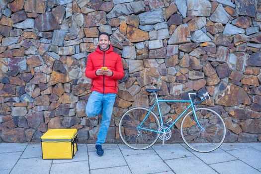 Food delivery concept. Young black man driver with backpack looking smart phone in the city to deliver products for customers who order online purchases. Black male happy with his job.