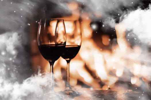 Winter atmosphere and Christmas holiday time, wine glasses in front of fireplace covered with snowy effect on window glass, holidays backgrounds
