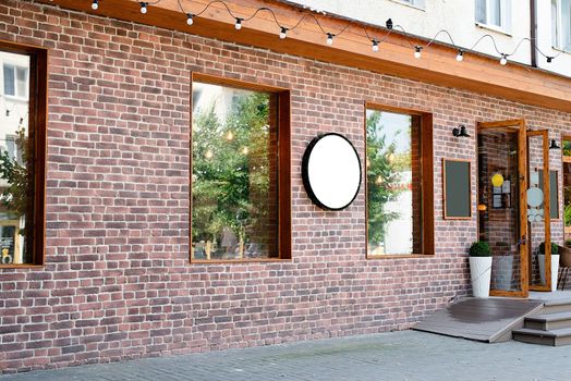 Cafe exterior in loft style with red brick wall, white round logo for mockup design. Cafe logo on red brick wall