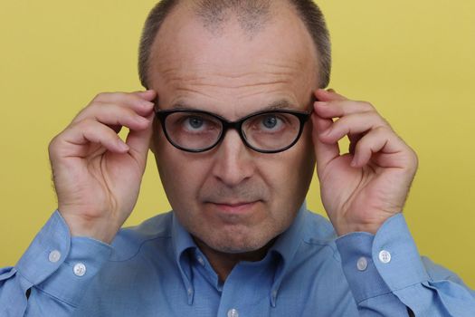 Man in blue shirt on yellow background holding transparent glasses.