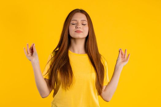 Calm woman relaxing, meditating, refuses stress. Sunny girl breathes deeply, calms down yellow studio background. Yoga, moral balance, zen concept. High quality photo