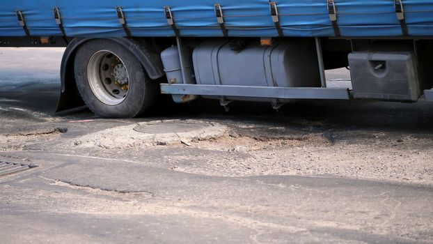 close-up, very poor road coverage, many pits, curved asphalt, a large truck slowly passes a stretch of road in disrepair. the road needs repair. High quality photo