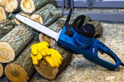 Close-up of a chain saw. electric chain saw and protective leather work gloves on the background of sawn tree trunks. lots of firewood. Firewood harvesting, forest clearing