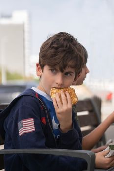 Portrait of a kid looking away stunned or surprised while eating a pancake in a park bench with his friend beside.