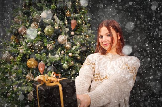 beautiful girl holding a box with a christmas present in her hand. Decorated Christmas tree on background. Christmas lifestyle with copy space