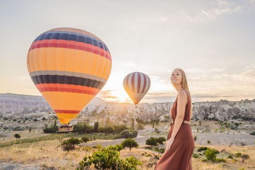 Tourist woman looking at hot air balloons in Cappadocia, Turkey. Happy Travel in Turkey concept. Woman on a mountain top enjoying wonderful view.