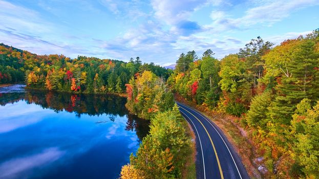 Image of Aerial over road next to blue lake and surrounded by fall forest