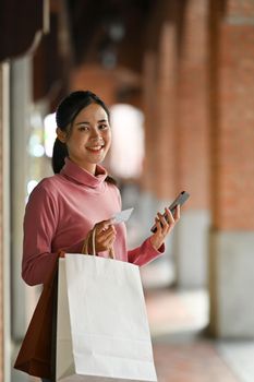 Smiling woman holding credit card and using smartphone for payment online.