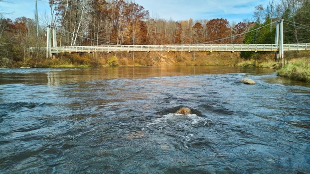 Image of At water level over river with view of suspension bridge in late fall