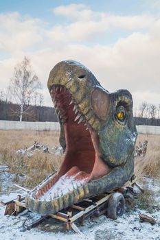 Abandoned huge head of decorative dinosaur on winter lawn.