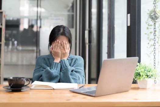 Young woman looks stressed, sitting at the desk, using a laptop, thinking and looking at the camera, feeling tired and bored with depression problems.