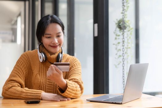 Attractive Asian female sits at her desk, holding a smartphone and a credit card. close-up image. Online payment, credit card payment, mobile banking, online shopping, cashless society...