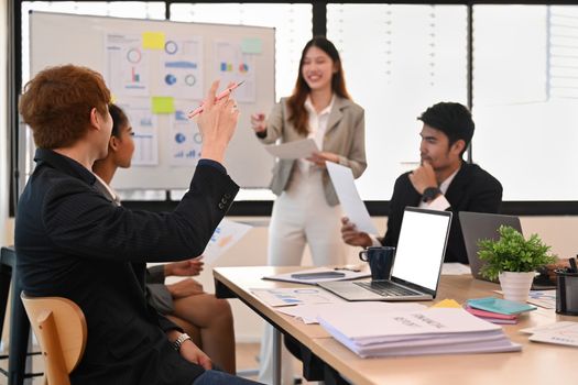 Asian businessman raise hand ask question to presenter, attending morning meeting in modern corporate office.