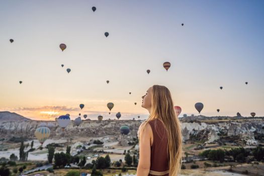 Tourist woman looking at hot air balloons in Cappadocia, Turkey. Happy Travel in Turkey concept. Woman on a mountain top enjoying wonderful view.