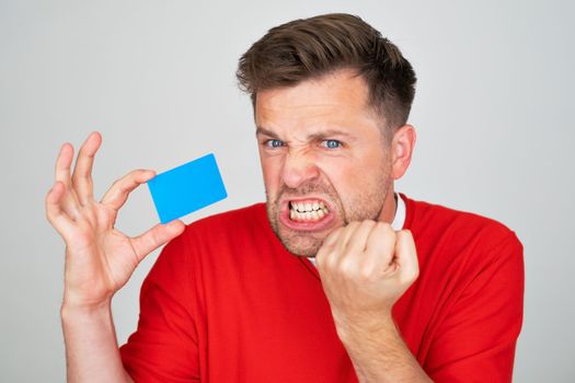 young handsome man feeling sad, upset or angry, frowning in disagreement with a credit card. 