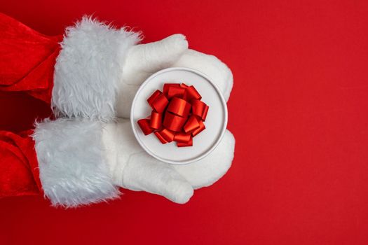 Santa's hands are holding a gift for Christmas. red background with space to copy. Christmas time