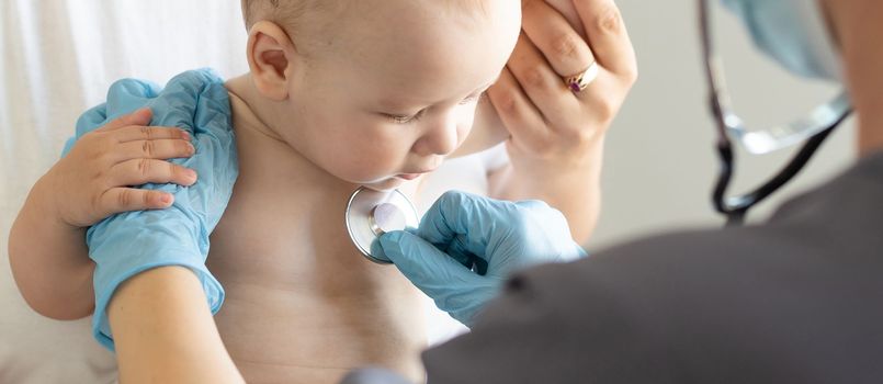 Female doctor examining little smiling baby girl, held by mother.