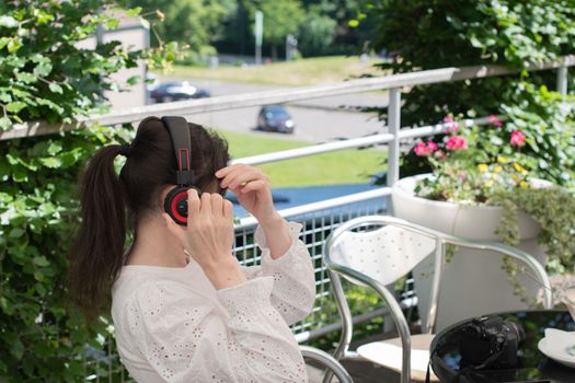 pensive brunette woman in a white blouse, listens to music on headphones at a table in a cafe, High quality photo