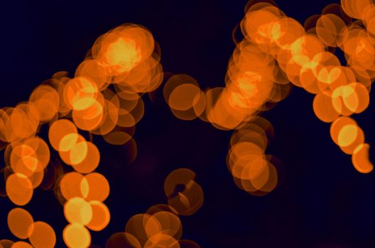 Enigmatic and romantic bokeh from blue glowing garlands. Festive new year lighting. Festive new year lighting Orange bokeh of electric garlands on a dark background.