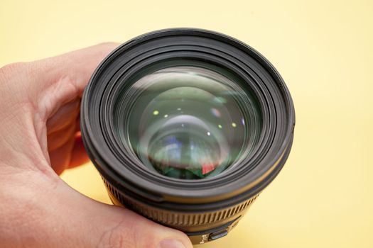 Close-up of a man holding a camera lens in his hand on a yellow background. 