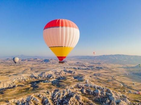 Colorful hot air balloons flying over at fairy chimneys valley in Nevsehir, Goreme, Cappadocia Turkey. Spectacular panoramic drone view of the underground city and ballooning tourism. High quality.