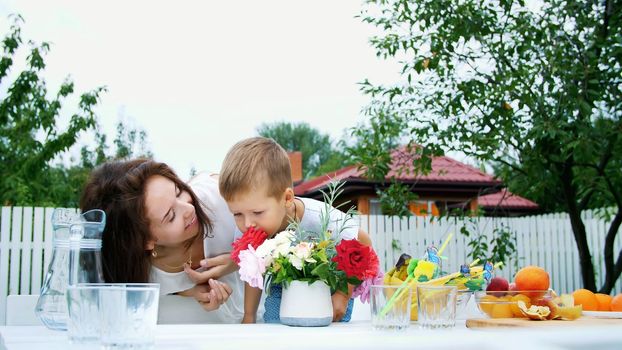 summer, in the garden. Mom with a four-year-old son make a bouquet of flowers. The boy likes it very much, having fun, sniffing flowers. The family spends their leisure time together. High quality photo