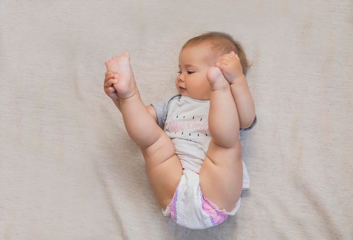 beautiful baby in a diaper lifted his legs to his head.