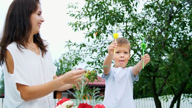 summer, in the garden, slow motion, Mom with a four-year-old son decorate the straw for juice. The boy likes it very much, he rejoices, has fun, shows his tongue. High quality photo