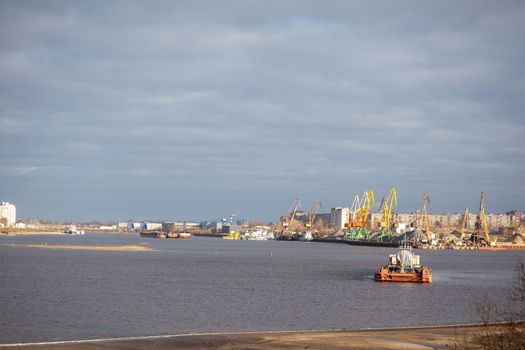 River port. Port cranes on the bank of the river. Embankment of the river port, a barge at the quay wall. Large port cranes on the river. Extraction and transportation of sand other cargo