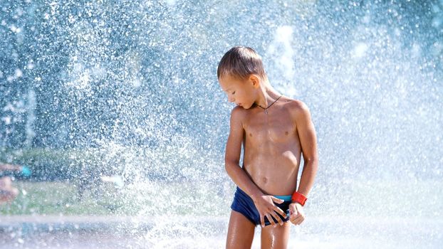 excited boy of seven years having fun between water jets, in fountain, run around, sprinkle, have fun, have fun, on a hot summer day. Summer in the city. Slow motion. High quality photo