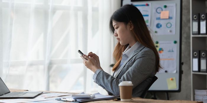 Beautiful asian businesswoman working with cell phone in office. business finance concept.