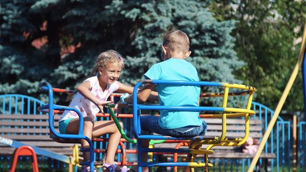 Happy children, a girl and a boy of seven, ride on a swing, on a hot summer day. Slow motion. Cheerful happy childhood, vacation. High quality photo