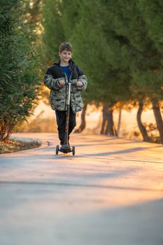 Boy riding scooter outdoor in the park on sunset.