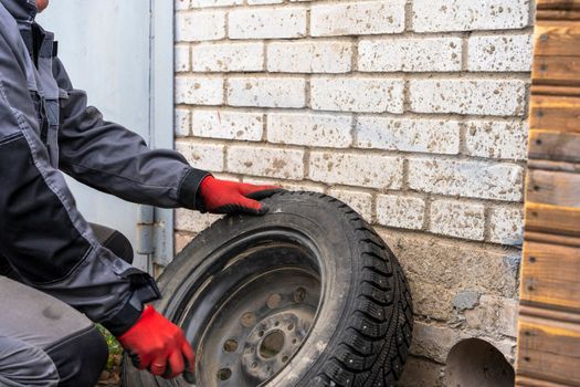 a male car mechanic in overalls inspects the wheel of a car. Car repair, seasonal replacement of car tires.