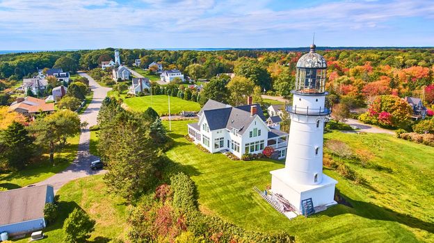 Image of Homes and fall forest surround pair of Maine Lighthouses on ocean