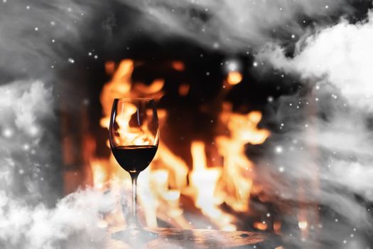 Winter atmosphere and Christmas holiday time, glass of wine in front of fireplace covered with snowy effect on window glass, holidays backgrounds